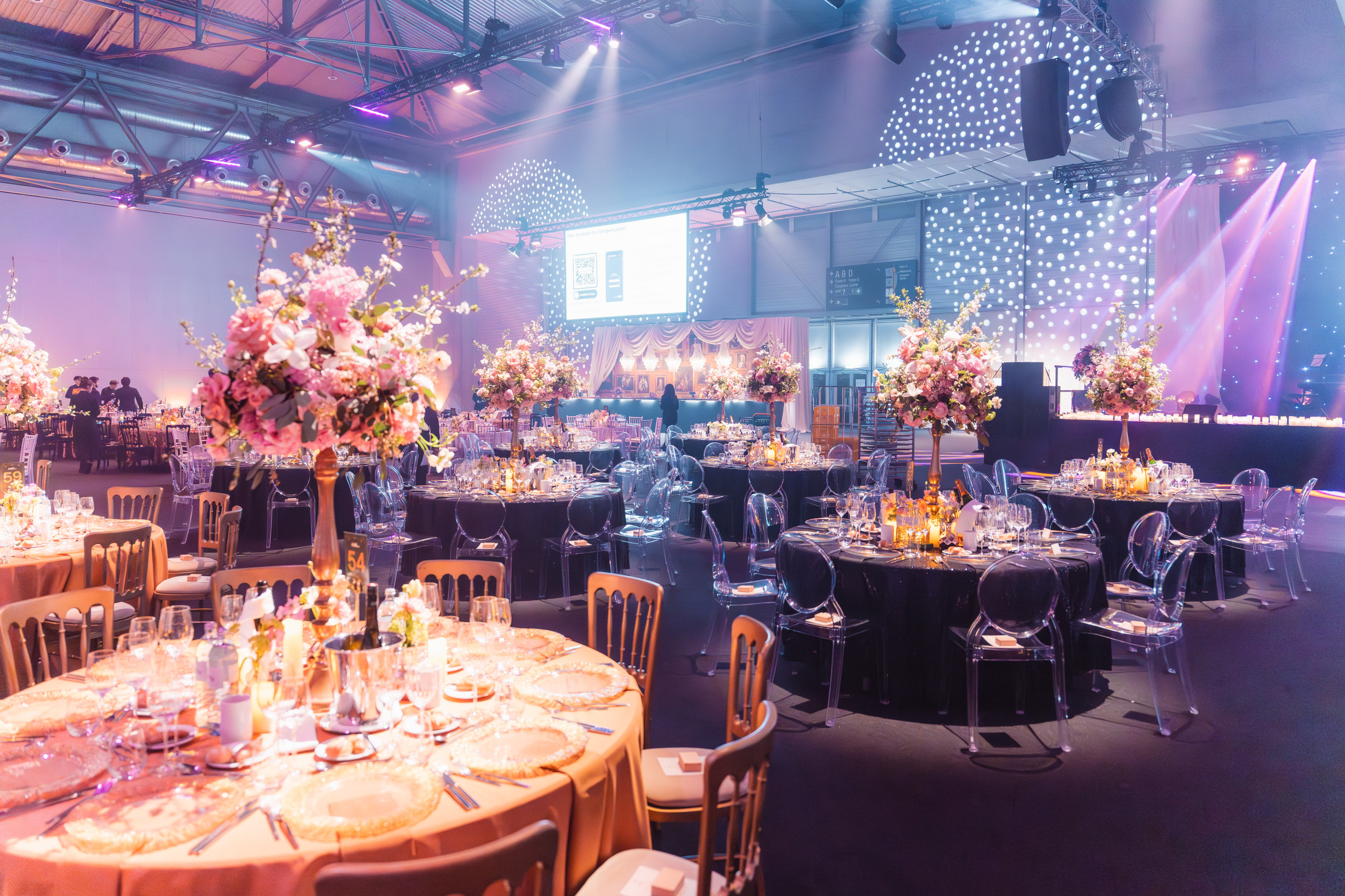 Elegant gala dinner setup at VIECON featuring round banquet tables, lavish floral centrepieces, atmospheric lighting, a stage area, and premium event décor for a large-scale evening event.